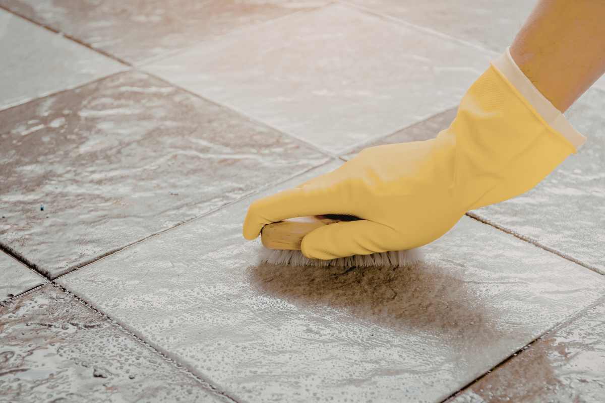 Hand cleaning shiny tile floor with yellow glove
