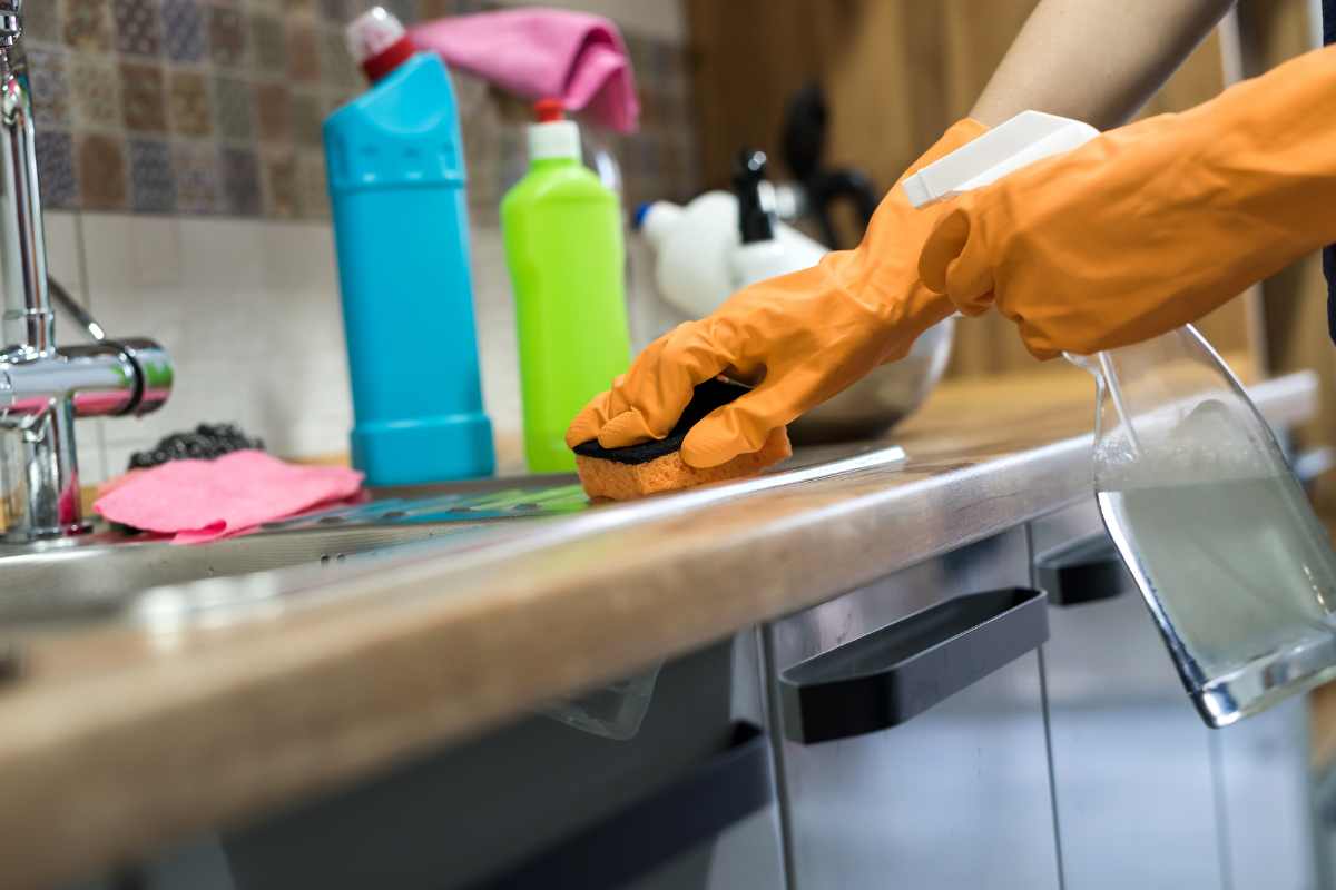 Woman wearing gloves cleaning kitchen cabinets and surfaces